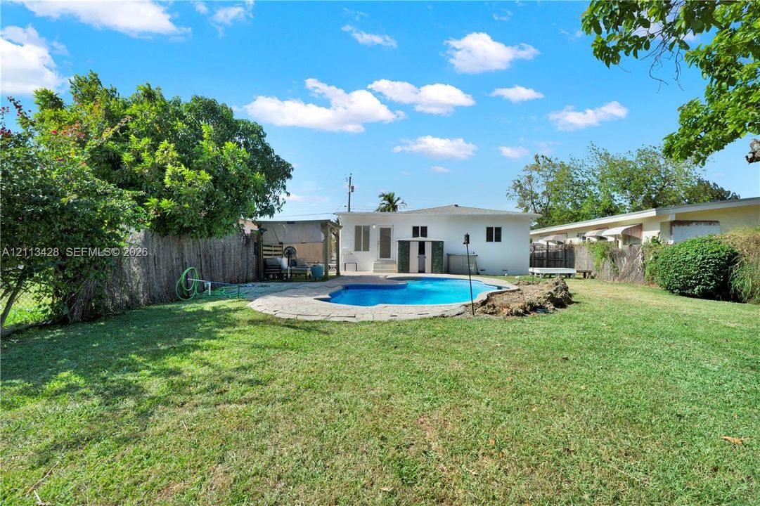 Backyard featuring a swimming pool, stone-paver decking, perimeter fencing, and mature trees