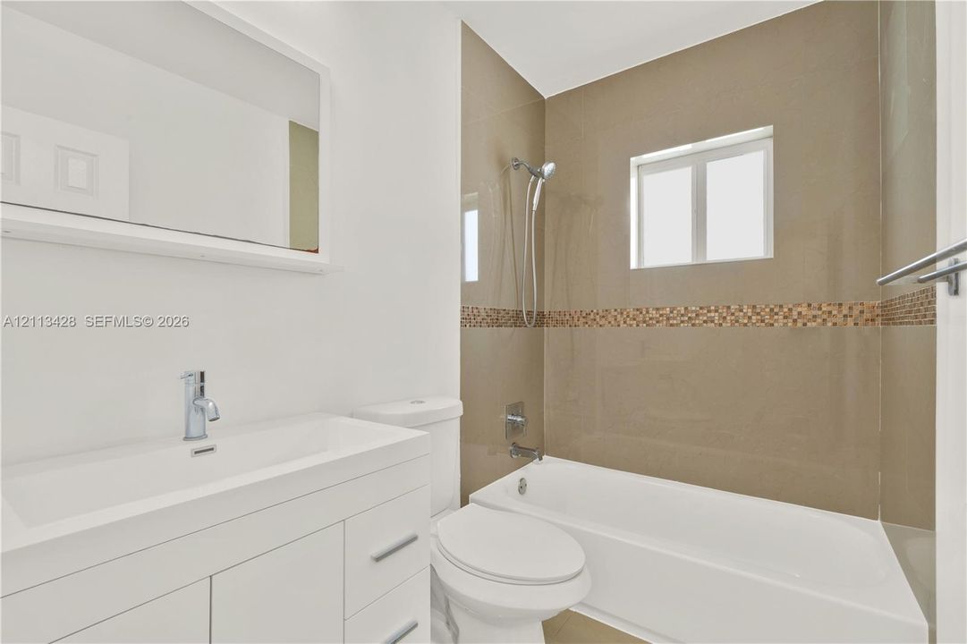 Bathroom featuring a white vanity with an integrated basin, a large wall-mounted mirror, a bathtub with a tiled shower surround, and a chrome hand-held shower fixture