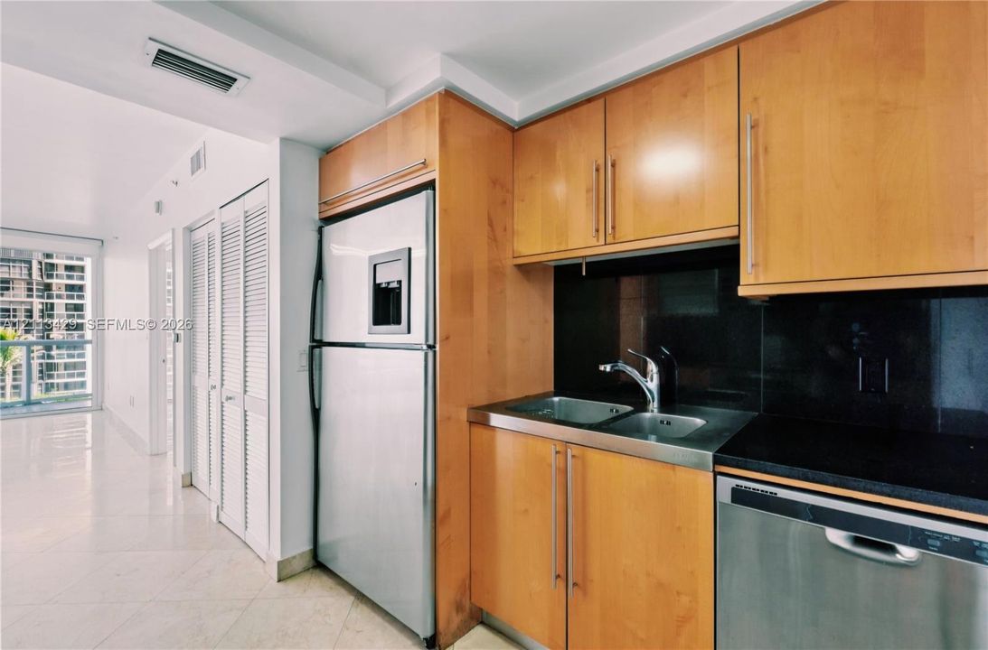 Kitchen featuring flat-panel wood cabinetry, black solid-surface countertops, dual-basin stainless steel sink with high-arc faucet, and stainless steel appliances