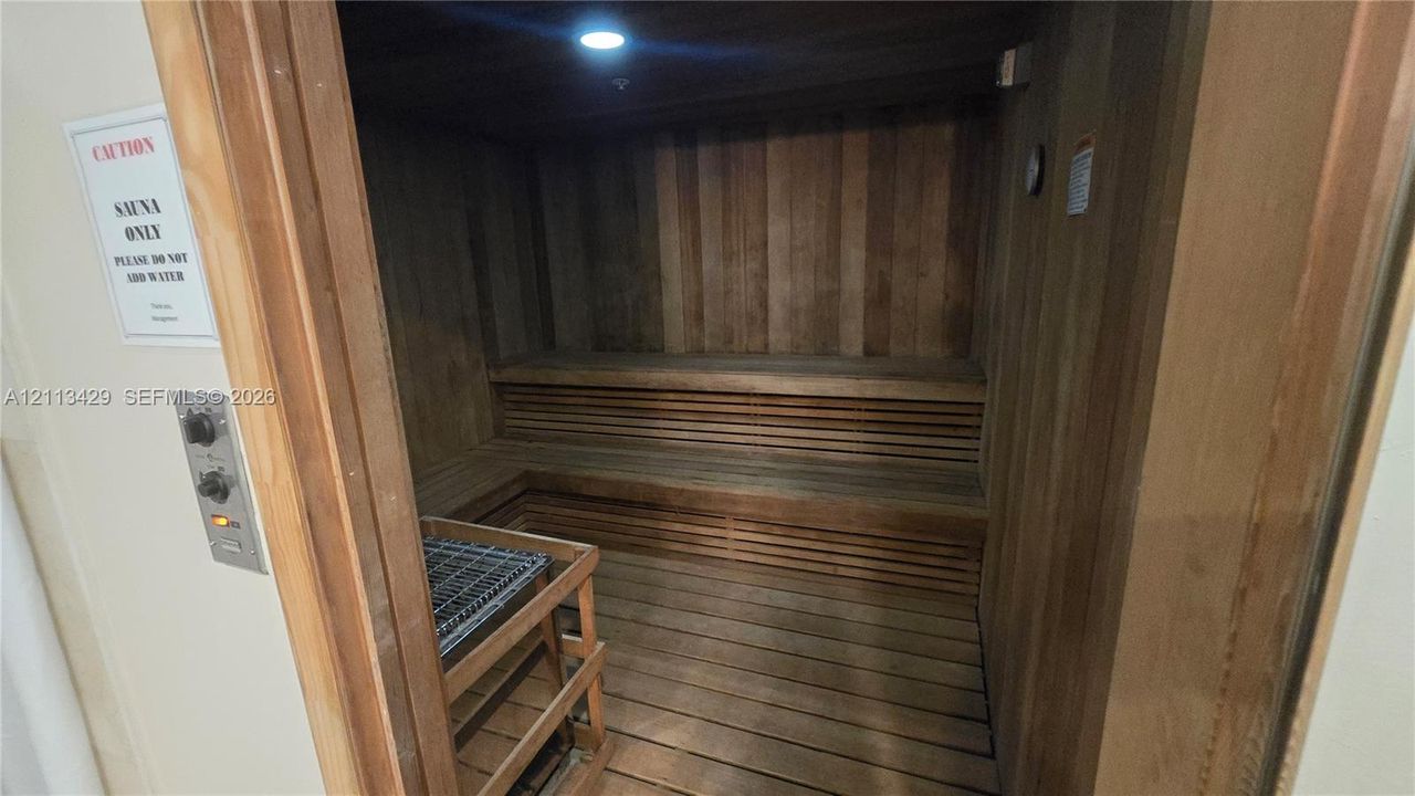 Sauna featuring wood-paneled walls, tiered bench seating, slated floorboards, and a recessed heating element