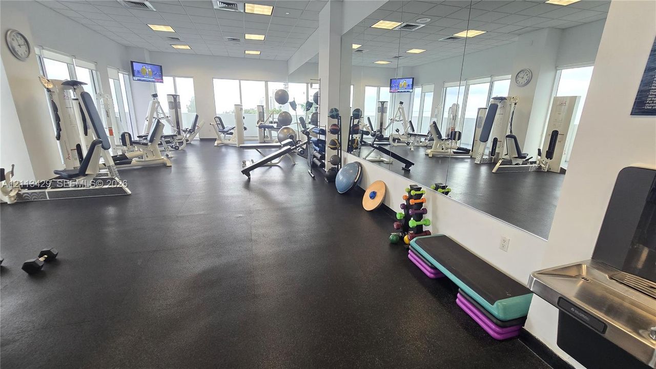 Fitness center featuring rubber flooring, floor-to-ceiling wall mirrors, recessed lighting, and a stainless steel wall-mounted water fountain