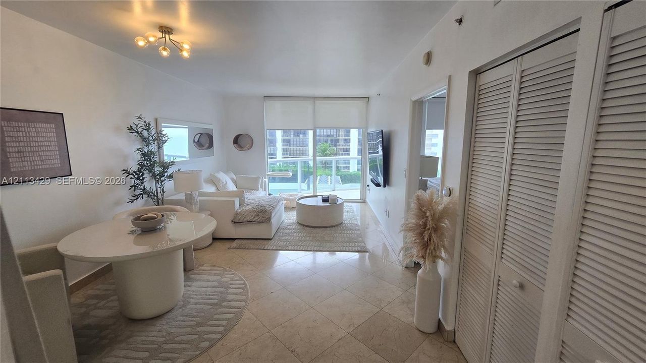 Living area featuring large-format tile flooring, louvered-style closet doors, glass sliding doors, and a multi-bulb flush-mount light fixture