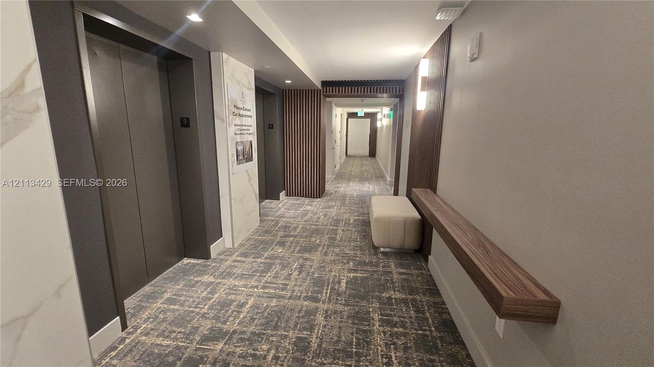 Elevator lobby featuring metallic elevator doors, stone-finish wall accents, vertical wood slat paneling, wall-mounted linear lighting, and a fixed wood-finish floating console