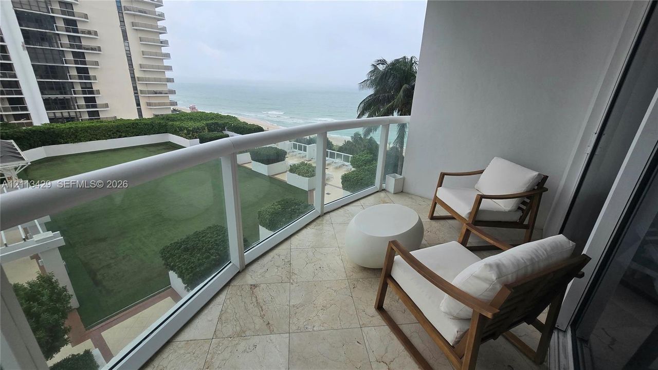 Balcony featuring stone tile flooring, a glass and metal railing, and an expansive ocean backdrop