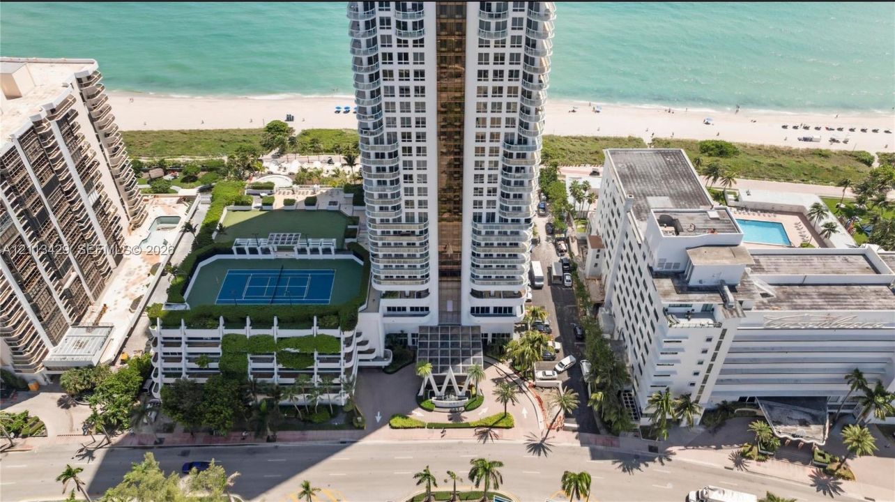High-rise building featuring direct beach access, an outdoor tennis court, and a multi-level parking structure
