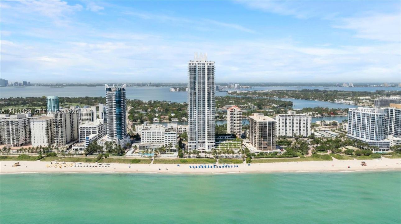 Aerial perspective featuring a direct beachfront location, high-rise architectural structures, expansive coastal shoreline, and surrounding waterfront scenery
