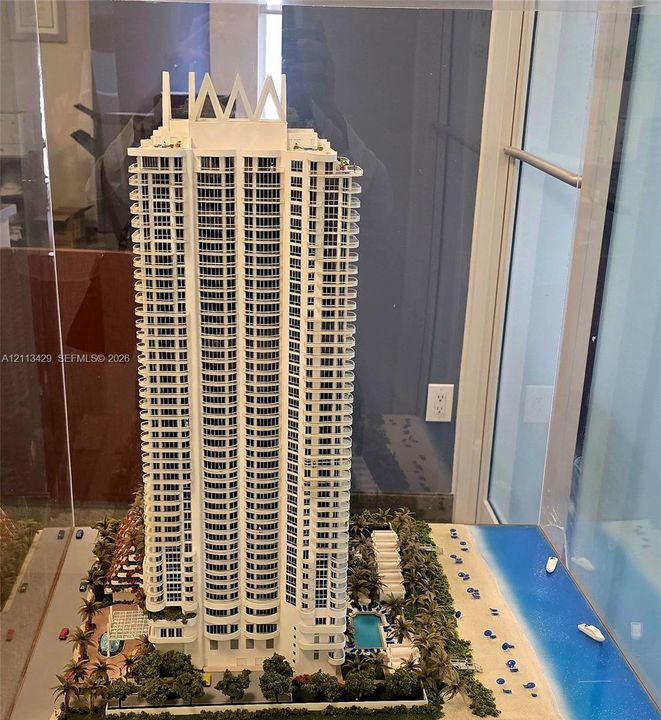 High-rise architectural model featuring wraparound balconies, an outdoor swimming pool, landscaped grounds, and immediate beach access