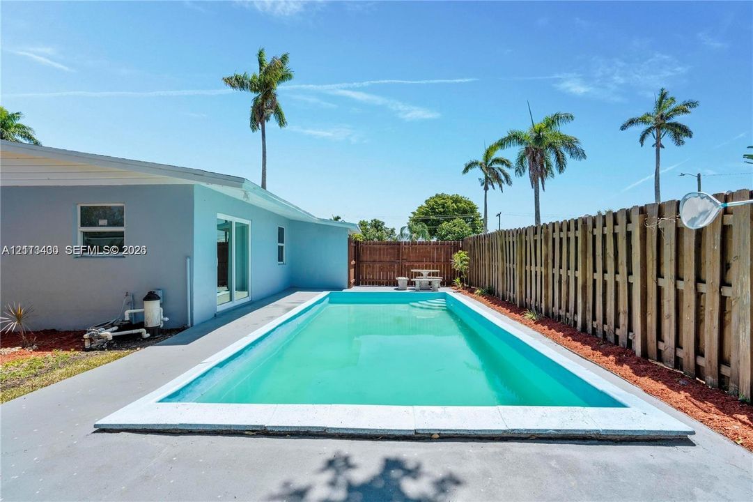 In-ground swimming pool with concrete decking, enclosed by a full-height wood privacy fence