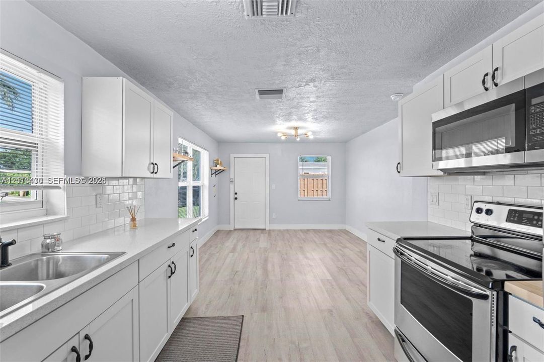 Kitchen featuring white shaker-style cabinetry, white subway tile backsplash, solid-surface countertops, stainless steel appliances, and wood-finish flooring
