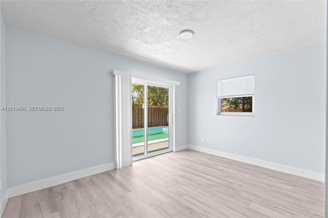 Interior space featuring light wood-finish flooring, sliding glass patio doors, and a window with a fitted blind