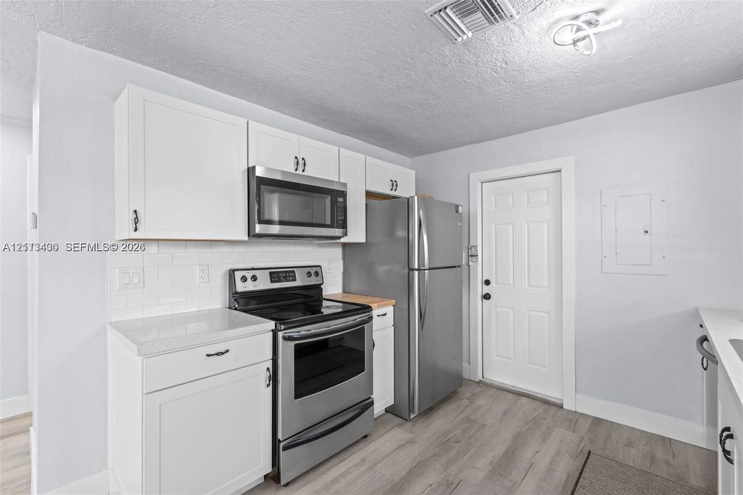 Kitchen featuring white cabinetry, subway tile backsplash, wood-finish flooring, and stainless steel appliances