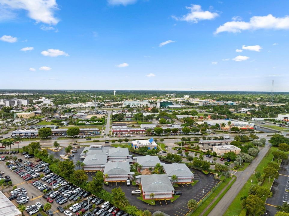 Aerial perspective of a multi-building property complex featuring paved parking surfaces, peripheral green space, and shingled rooflines