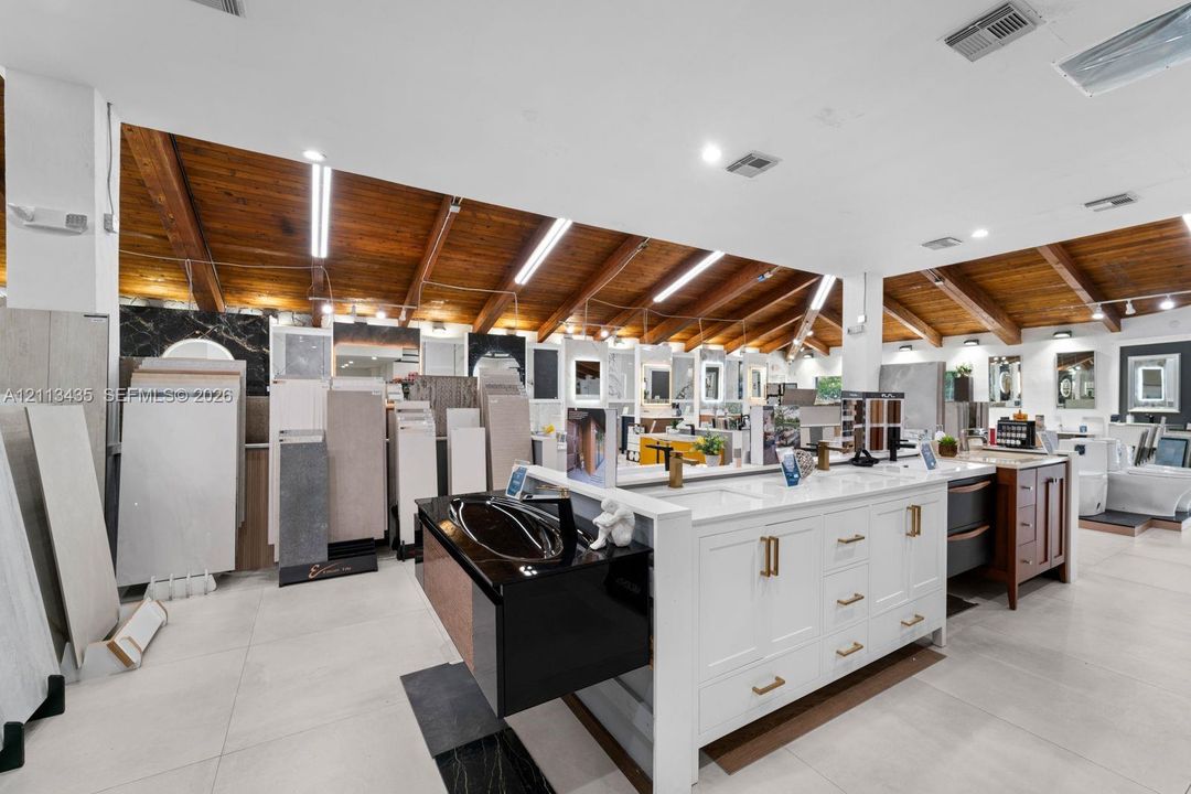Vaulted ceiling with exposed wood beams, white cabinetry, integrated stone countertops, and polished large-format tile flooring