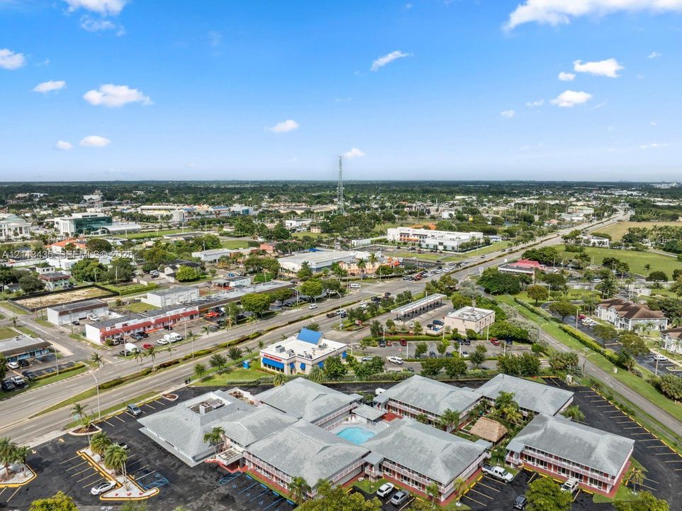 Aerial perspective of a multi-building commercial complex featuring a central courtyard swimming pool, extensive surface parking, and shingled roof structures
