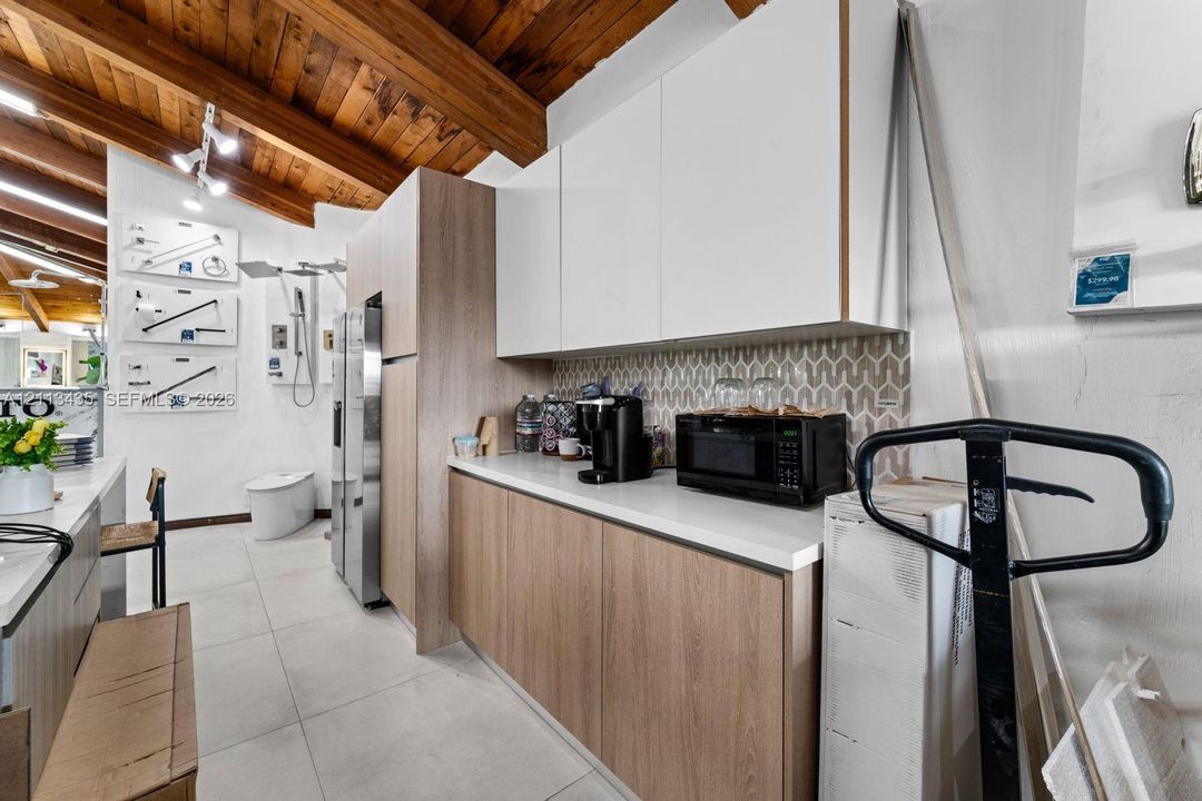 Exposed wood-beam ceiling, flat-panel cabinetry in matte white and wood-finish, geometric patterned tile backsplash, solid-surface countertops, and large-format porcelain tile flooring