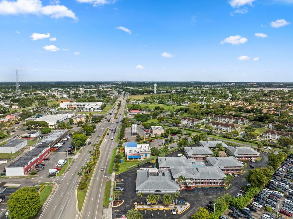 Aerial perspective featuring a multi-building commercial complex with asphalt parking areas and mature landscaping