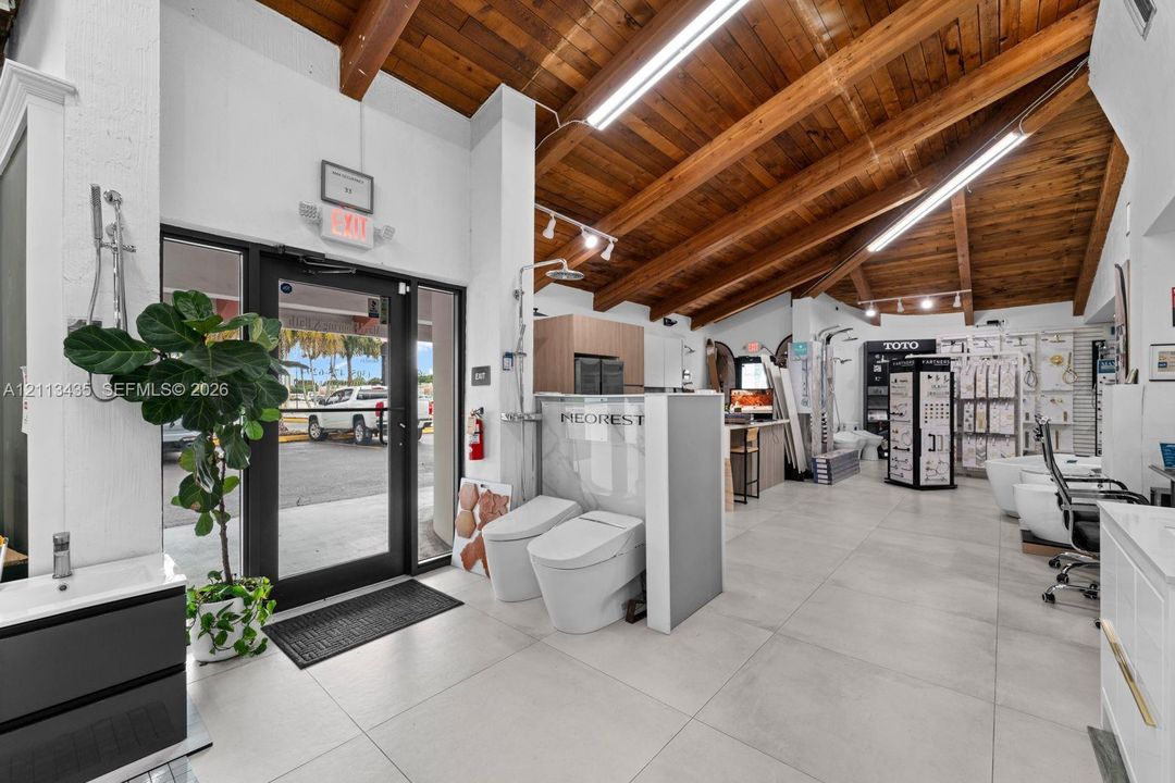 Vaulted ceiling with exposed wood beams, large-format tile flooring, and floor-to-ceiling glass entry door
