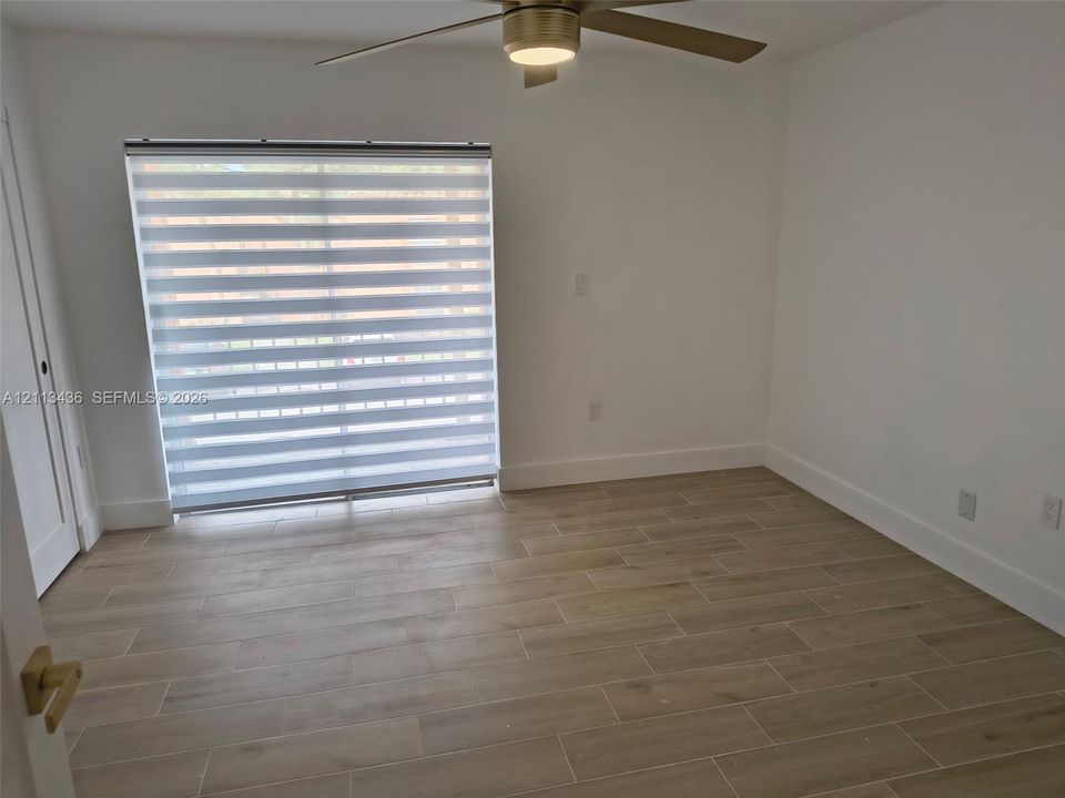 Wood-finish tile flooring, ceiling fan with integrated light, and sliding glass door with horizontal blinds