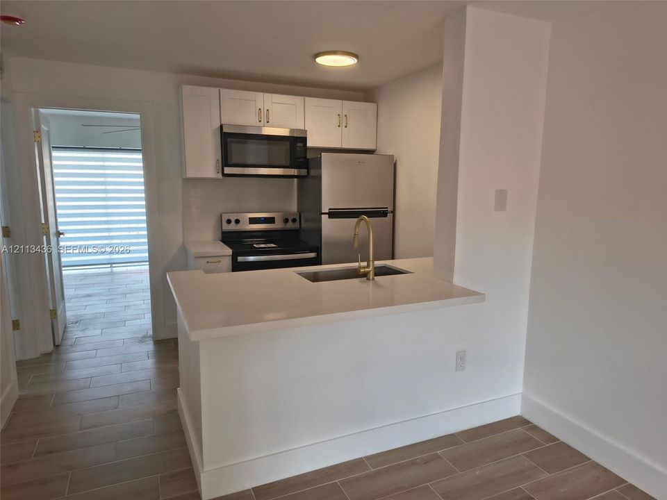 Kitchen featuring white shaker-style cabinetry, quartz countertops, stainless steel appliances, a brass-finish arched faucet, and wood-finish flooring