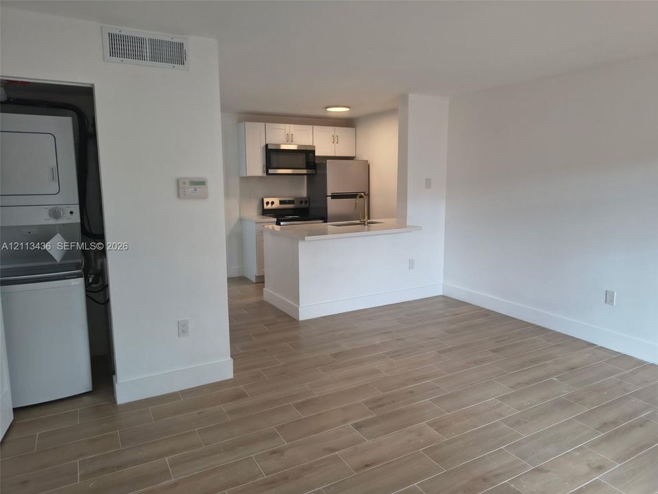 Kitchen featuring white shaker-style cabinetry, a breakfast bar with stone-finish countertops, stainless steel appliances, and wood-finish tile flooring throughout