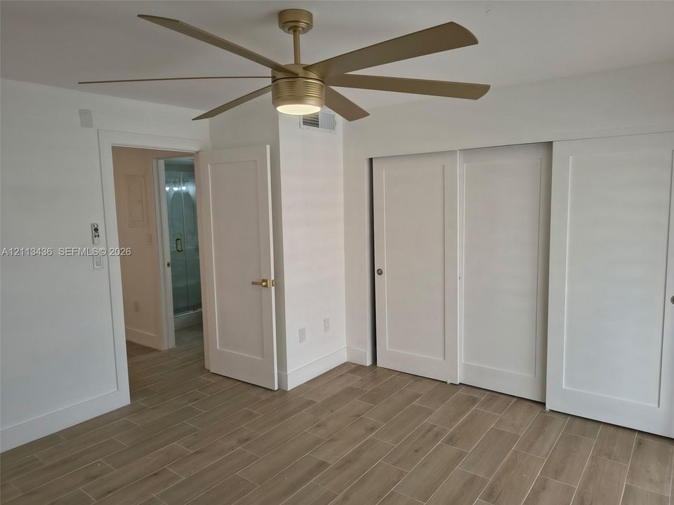 Wood-finish flooring, matte gold-tone multi-blade ceiling fan with integrated lighting, and three-panel sliding closet doors