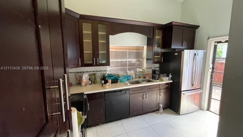 Kitchen featuring dark wood cabinetry, light-toned countertops, tile flooring, glass-paneled upper cabinets, and stainless steel appliances