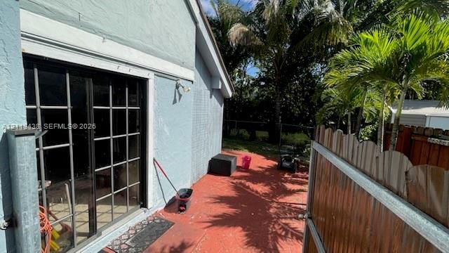 Exterior patio featuring a painted concrete floor, sliding glass doors with grid detailing, and a wooden privacy fence