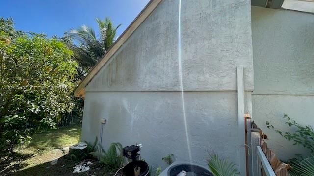 Stucco exterior siding with gable roof line, integrated HVAC unit, and mature landscaping