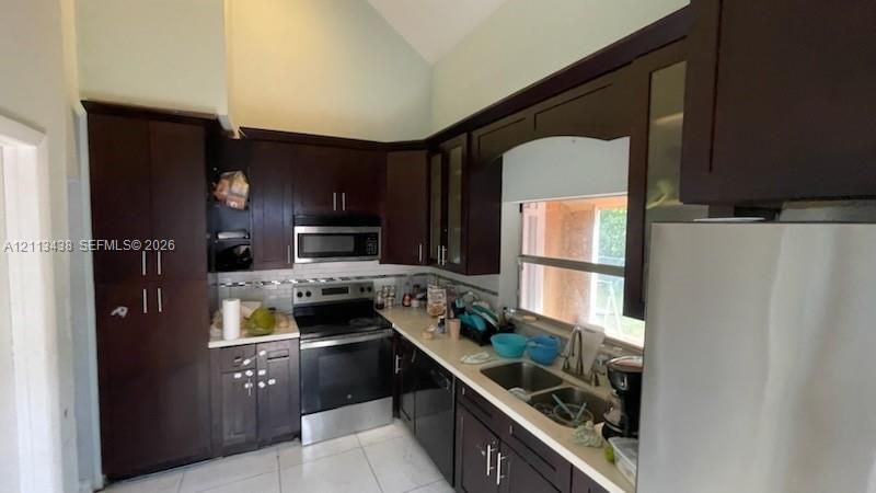 Kitchen featuring dark wood cabinetry, stainless steel appliances, vaulted ceiling, and light-toned countertops