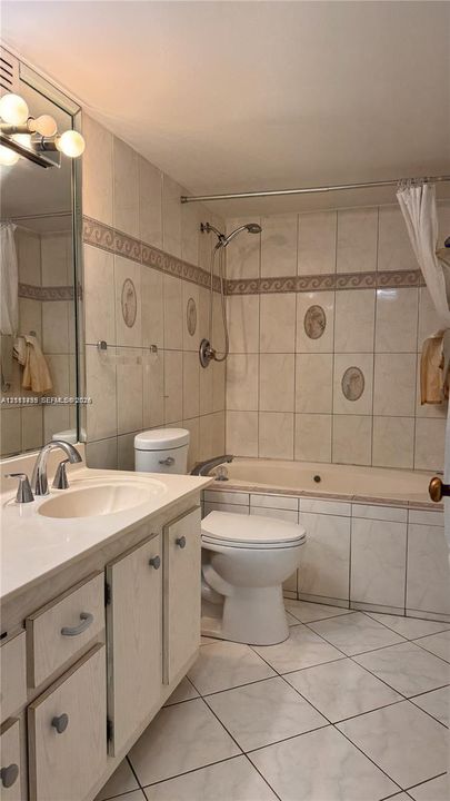 Bathroom featuring a vanity with an integrated basin, a soaking tub with a wall-mounted handheld shower fixture, tiled surround with decorative accents, and tiled flooring