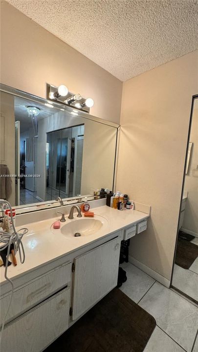 Vanity featuring a light-toned wood-finish cabinet, integrated countertop with a circular basin, chrome-finish faucet, full-width wall-mounted mirror, and three-bulb vanity light fixture
