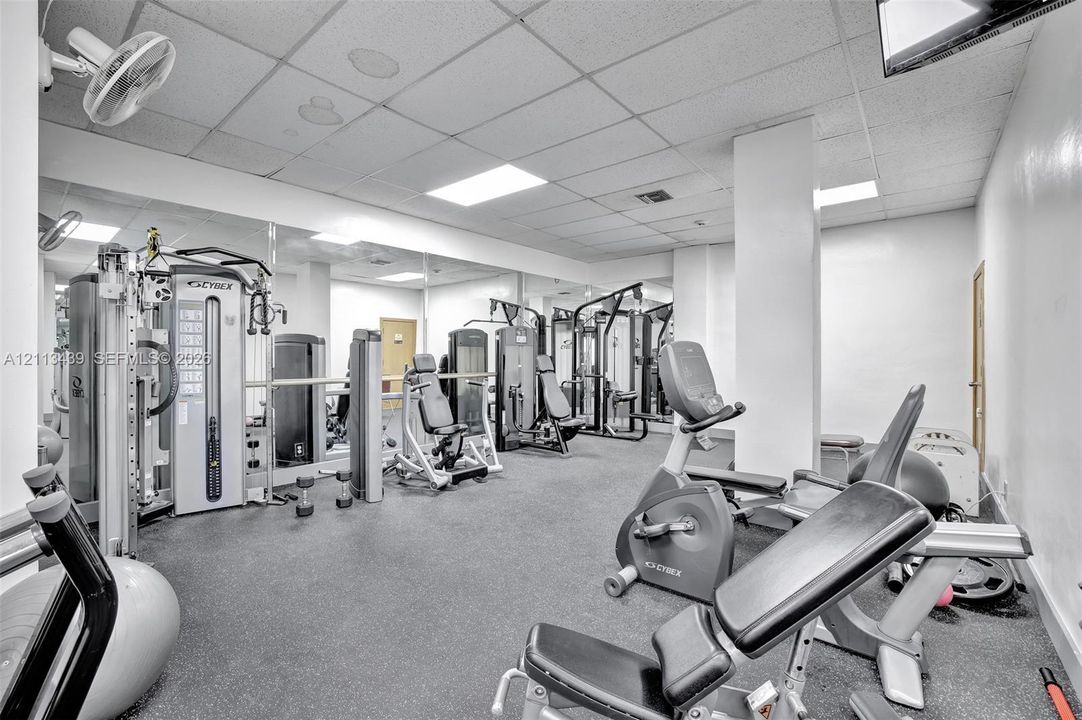 Fitness facility featuring wall-to-wall mirrors, recessed lighting, drop ceiling, and rubberized flooring
