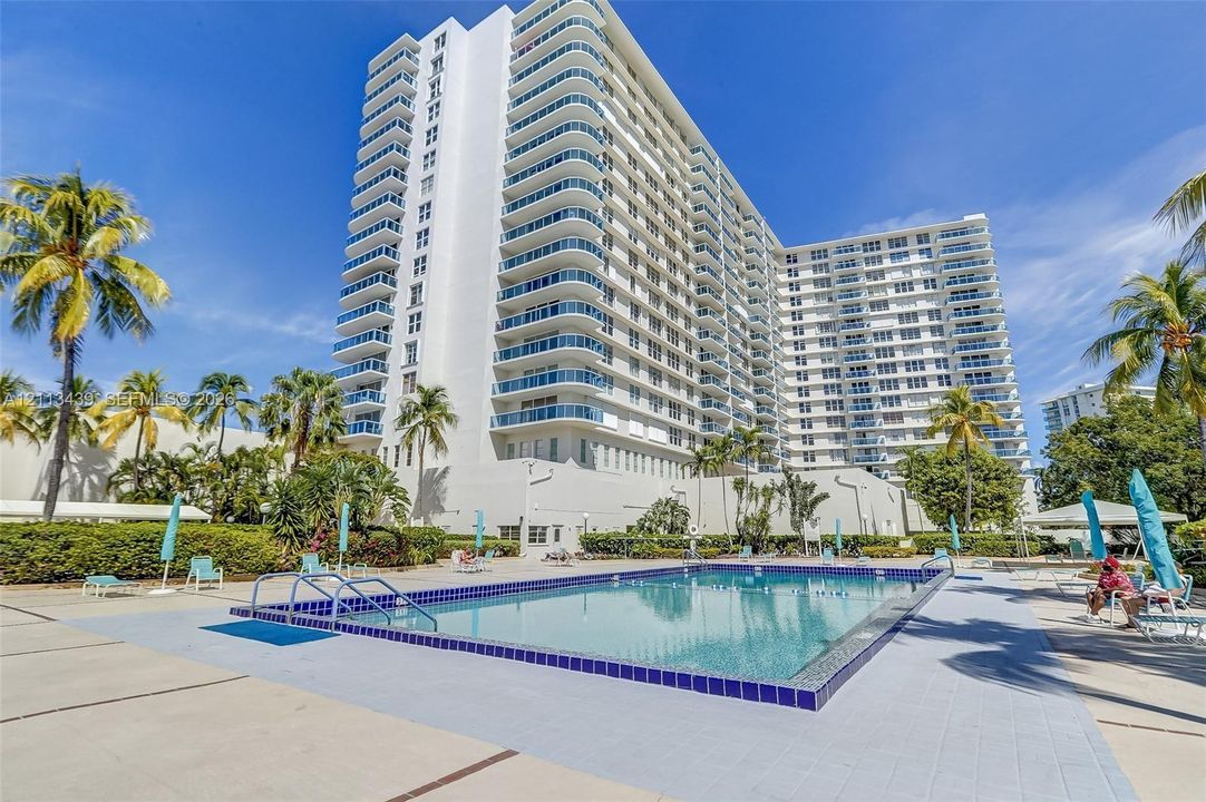 High-rise residential exterior featuring private glass-railed balconies and a ground-level rectangular swimming pool with tile trim and concrete decking