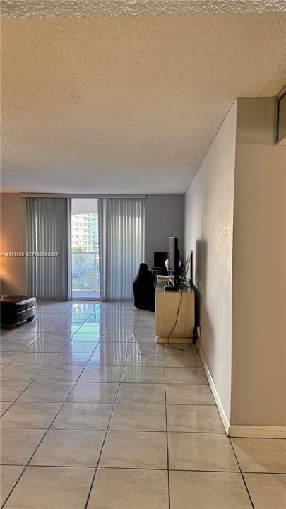 Open interior space featuring light-toned tile flooring and full-height vertical blinds leading to an exterior balcony