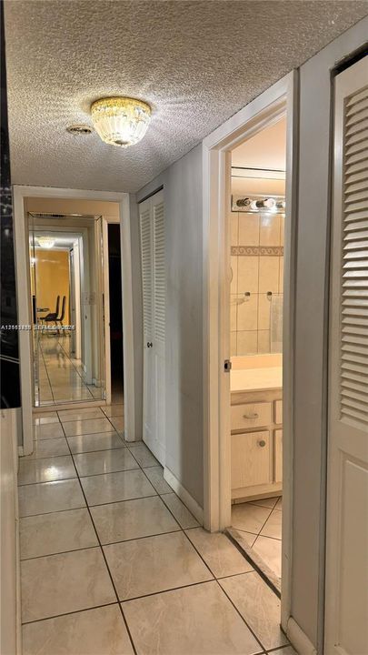 Hallway featuring ceramic tile flooring, built-in louvered-door closets, and a decorative flush-mount ceiling light