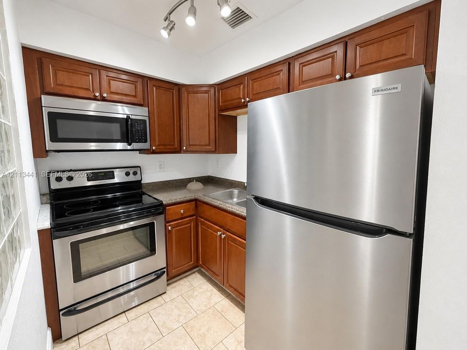 Kitchen featuring stainless steel appliances, wood cabinetry, stone-finish countertops, ceramic tile flooring, and adjustable track lighting