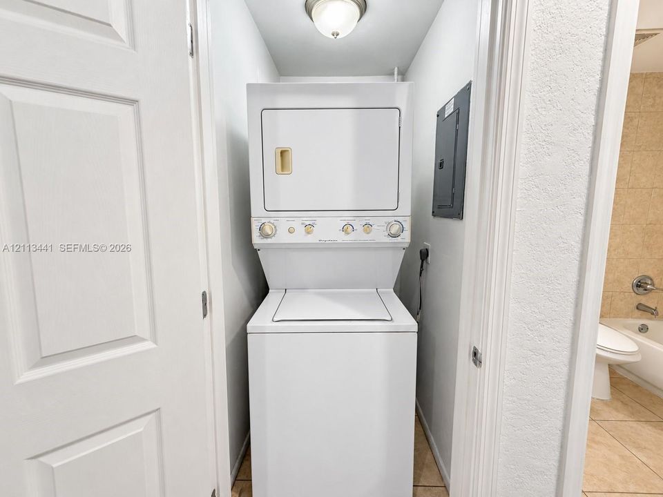 Stackable laundry center featuring a top-loading washer and front-loading dryer, flush-mount ceiling light fixture, and tile flooring