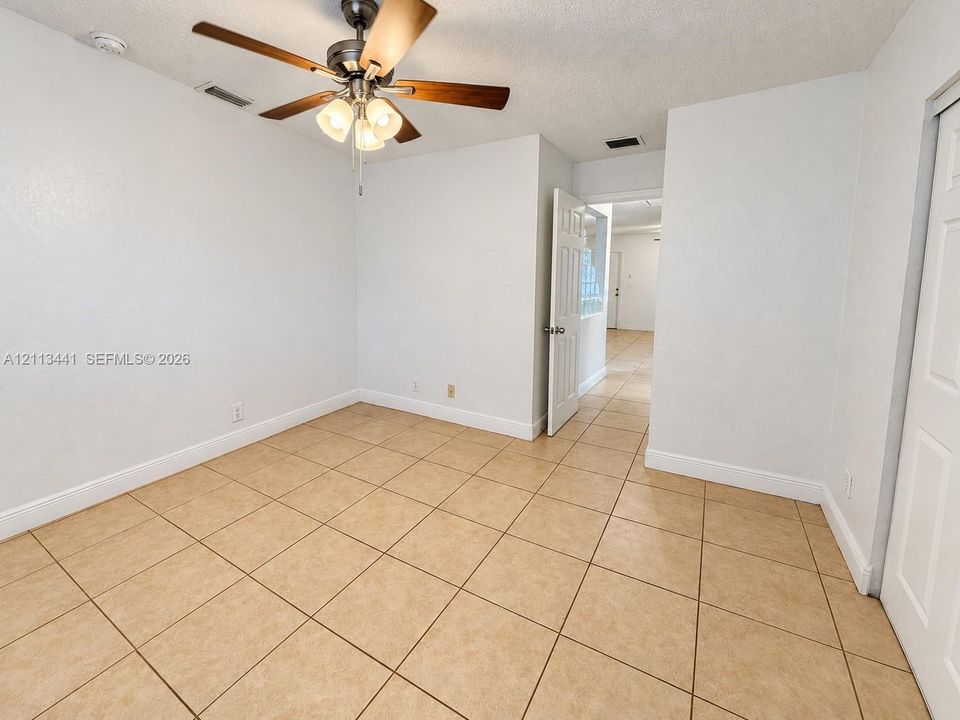 Neutral-toned ceramic tile flooring, ceiling fan with integrated three-light fixture, and white panel doors