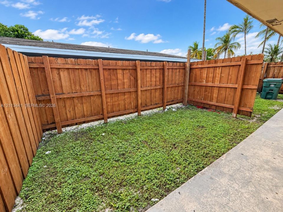 Outdoor space featuring a concrete patio, wood privacy fencing, and a grass lawn