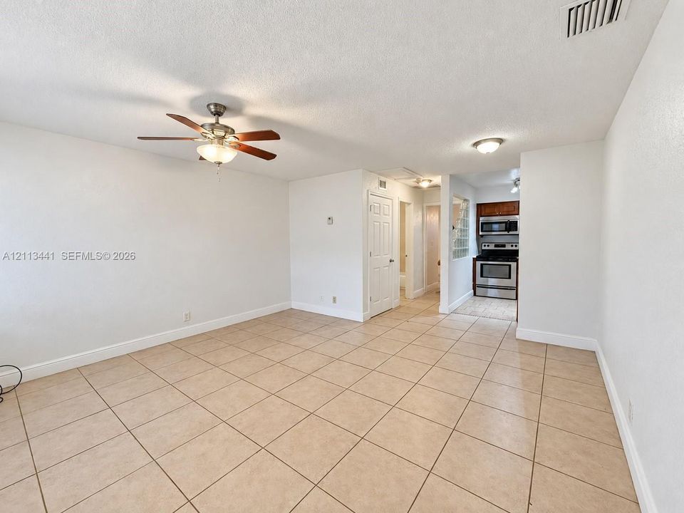 Open-concept interior featuring large-format neutral tile flooring, ceiling fan with integrated light fixture, recessed lighting, and kitchen equipped with stainless steel appliances
