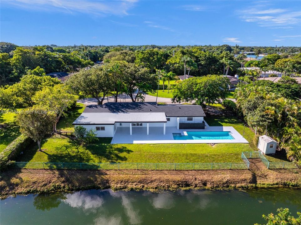 Waterfront property featuring a swimming pool, covered patio, expansive lawn, and mature trees