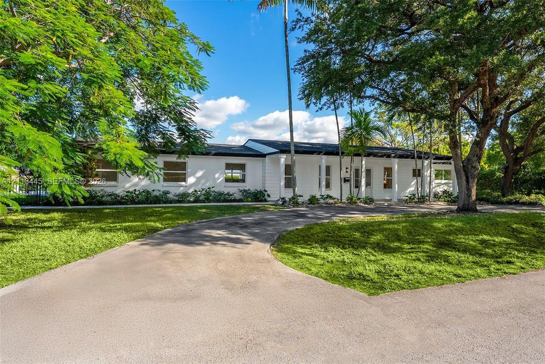 Single-story residence featuring a painted masonry exterior, covered entryway with structural columns, and a paved driveway, set upon a lot with mature trees and established landscaping