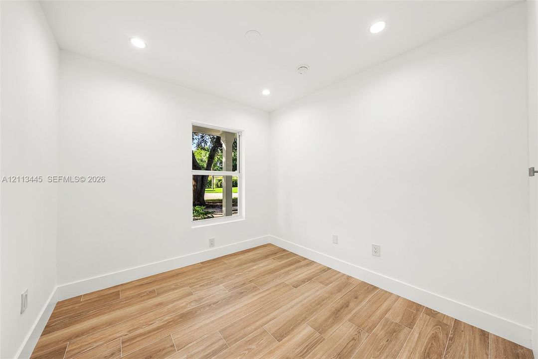 Room featuring wood-finish flooring, recessed lighting, and a single window with exterior greenery