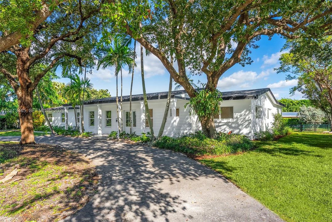 Single-story residence featuring a white painted exterior, asphalt driveway, mature canopy trees, and established landscaping
