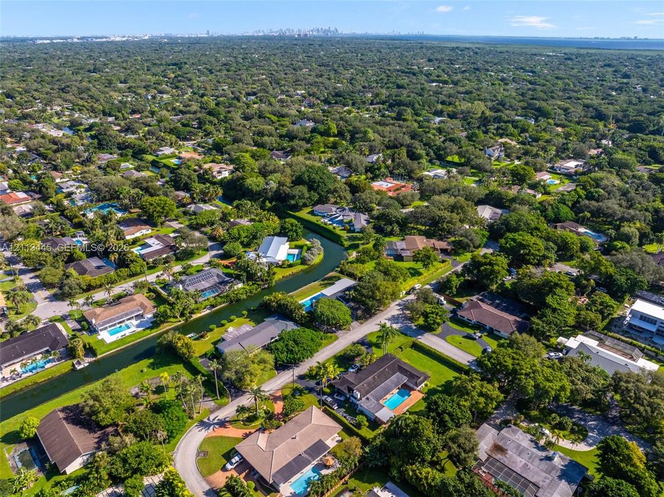 Aerial perspective of a residential neighborhood featuring mature tree canopies, paved street infrastructure, and multiple properties with private swimming pools and water-front canal access