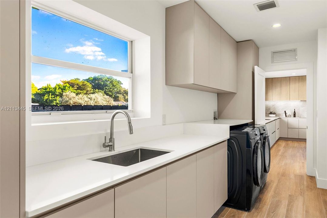 Utility room featuring solid-surface countertops, undermount stainless steel sink, pull-down faucet, flat-panel cabinetry, and wood-finish flooring