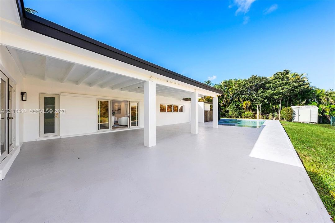 Covered patio featuring an expansive concrete surface, support columns, sliding glass doors, a built-in swimming pool, and a manicured lawn