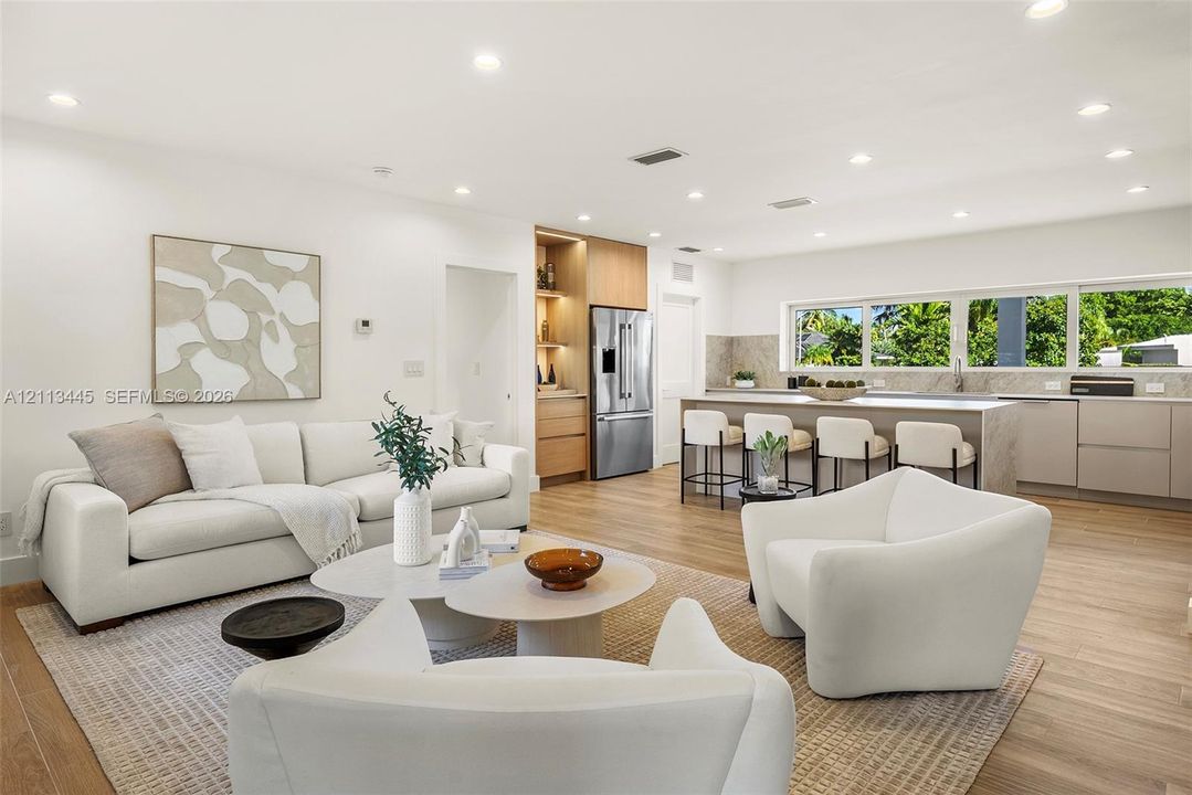 Open-concept kitchen featuring an expansive center island, integrated cabinetry, stainless steel appliances, and wood-finish flooring illuminated by recessed lighting