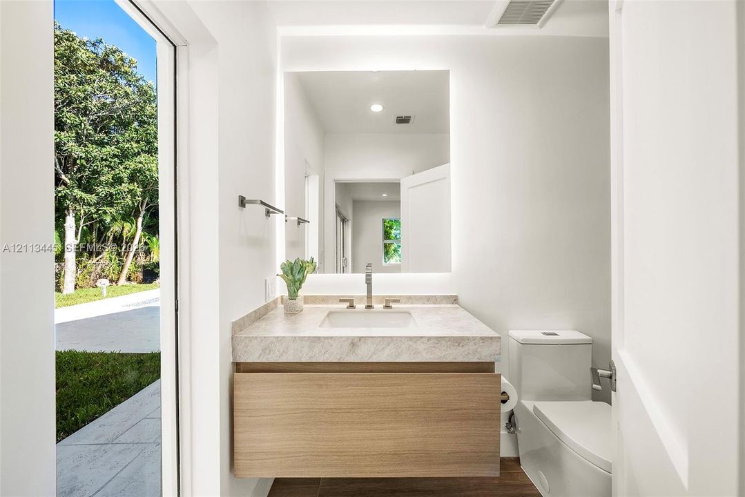 Floating wood-finish vanity with a stone countertop, rectangular undermount sink, integrated backlit mirror, and dual-flush toilet