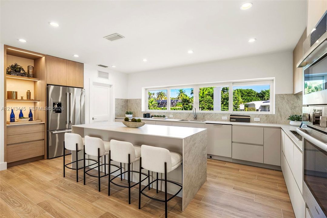 Kitchen featuring flat-panel cabinetry, a central island with a stone-finish countertop, wood-finish flooring, recessed lighting, and stainless steel built-in appliances